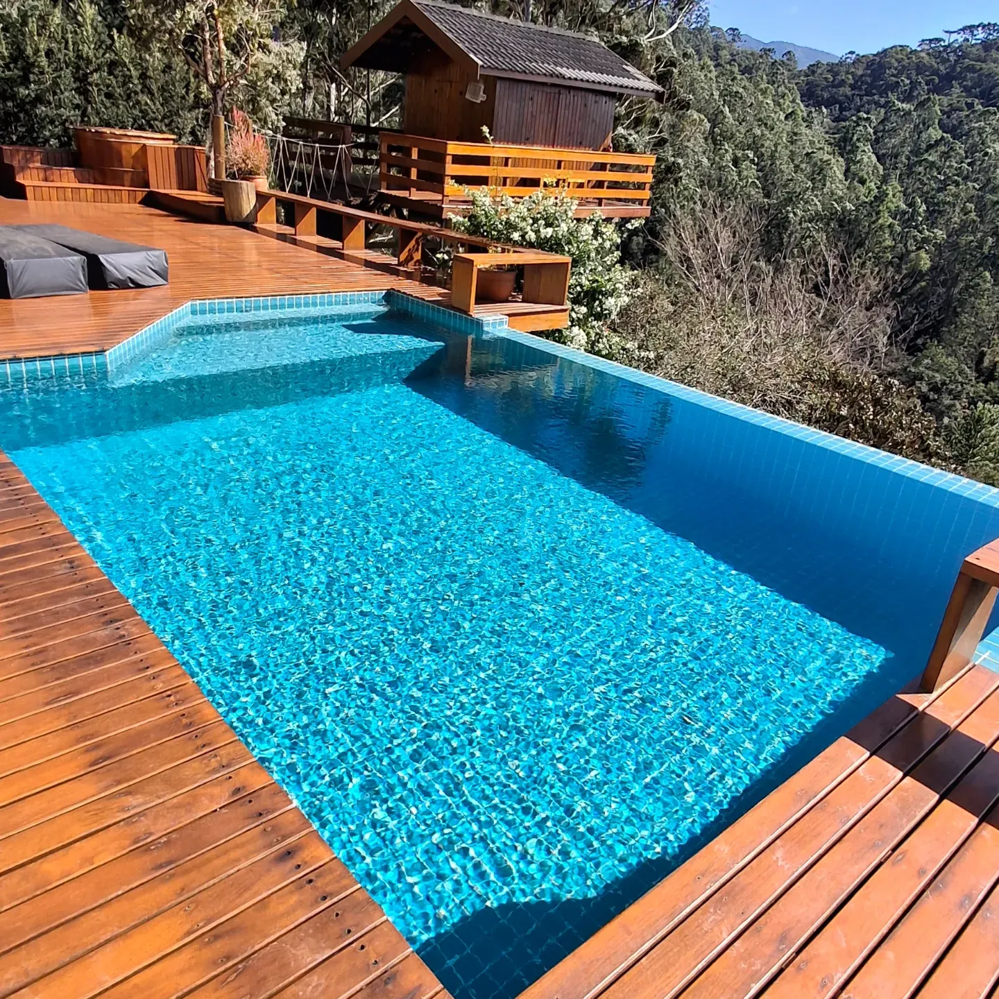 Piscina azul com deck de madeira e mata da serra ao fundo
